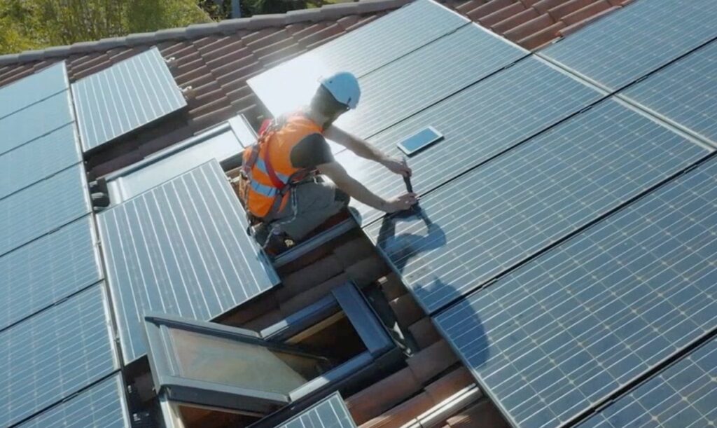 Man på som installerar solceller på tak med säkerhetsutrustning.
